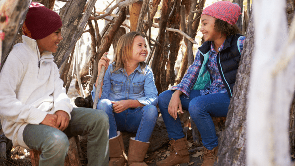 Three children sitting in a woodland den they’ve built