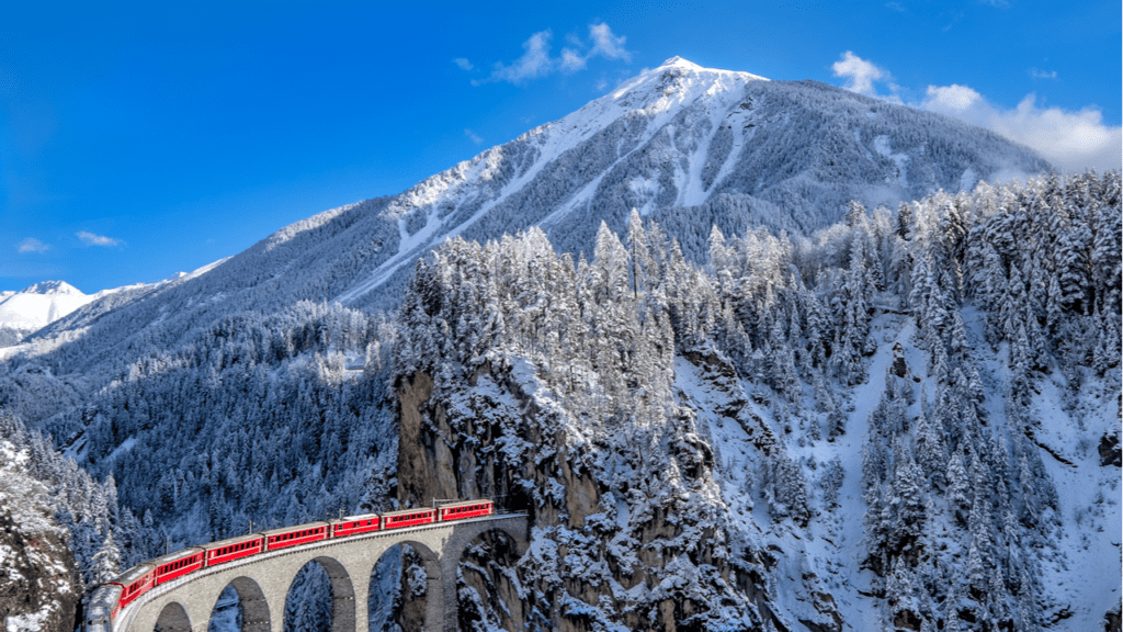 The Glacier Express in Switzerland passing over a viaduct in a snowy, mountainous landscape