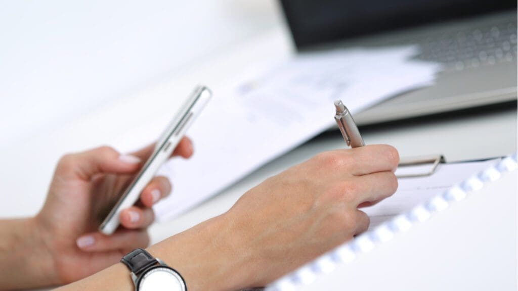 A person taking notes while looking at a phone screen