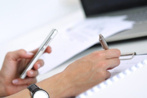 A person taking notes while looking at a phone screen